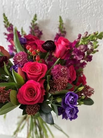 Jewel toned flower bouquet with roses, lisianthus, snapdragons, ranunculas and skimmia. 