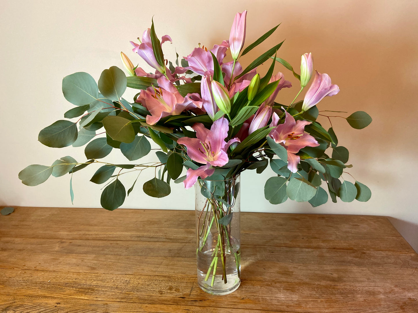 Pink oriental lilies with silver dollar eucalyptus in a vase. 